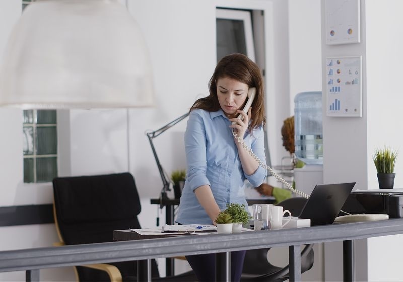 Una chica en su mesa de trabajo hablando por teléfono fijo.